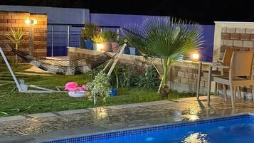 Una piscina con borde de azulejos, rodeada de un muro de ladrillo, césped y plantas en macetas.
