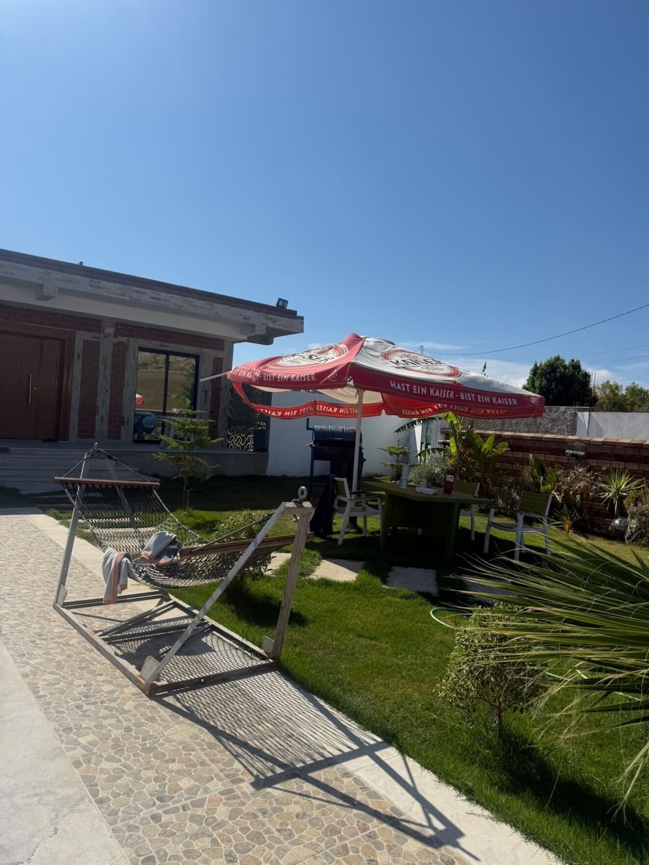 Un patio con una hamaca, una mesa con sillas y una parrilla.
