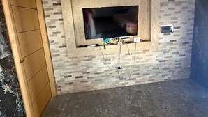Quarto com parede revestida em azulejos, porta de madeira e televisão de tela plana fixada na parede.