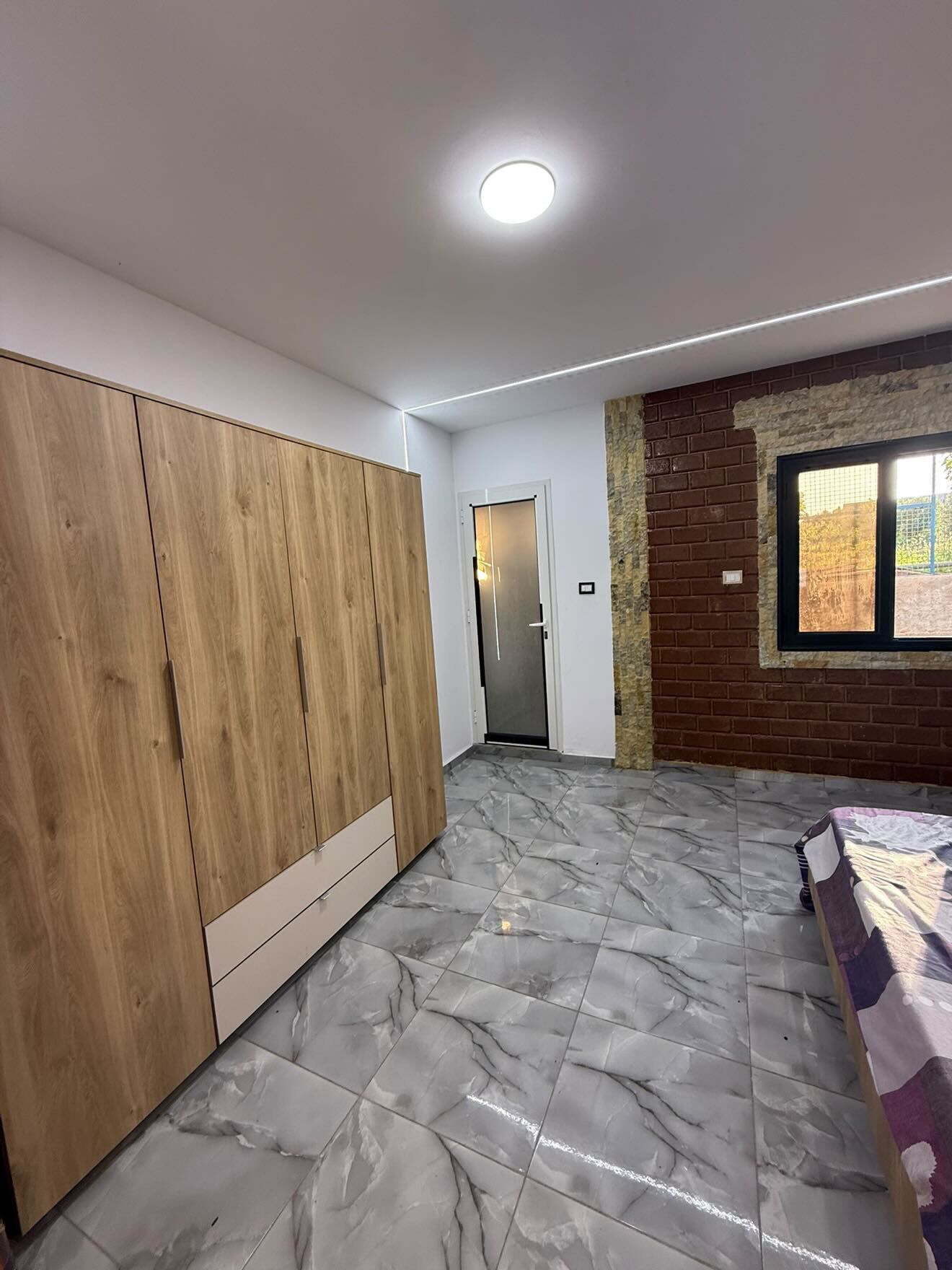 Een kamer met een inbouwkast, een deur, een bakstenen muur en een raam.