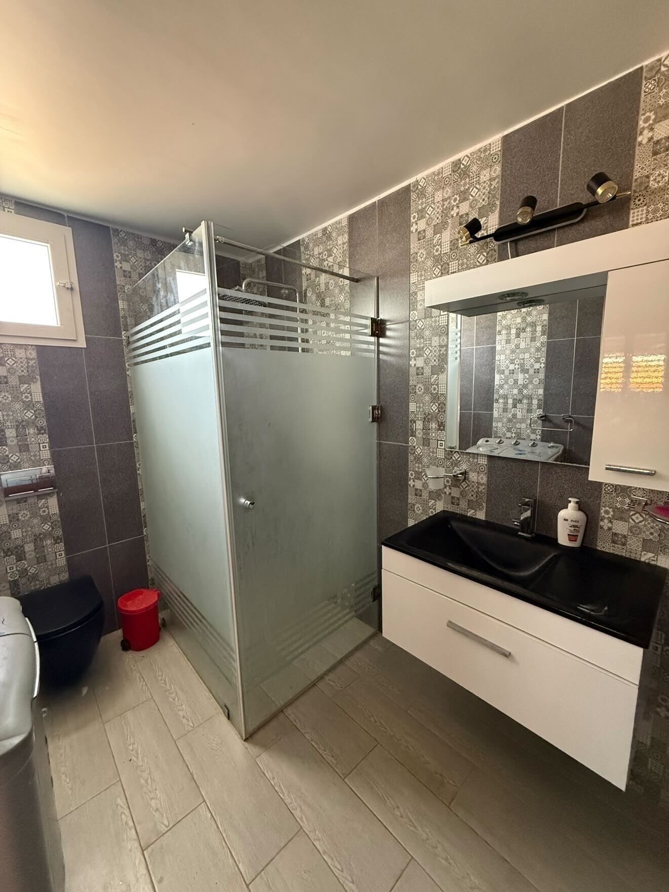 A modern bathroom with a glass shower enclosure, a black sink, and patterned tiles.