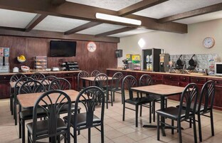 Un restaurante con mesas y sillas de madera, una zona de cocina y un televisor montado en la pared.