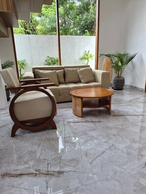 Una habitación con un sofá, una mesa redonda de madera, una silla y una planta en maceta.