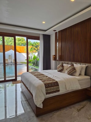 Una cama grande con un edredón estampado, un cabecero de madera y vistas a una piscina a través de puertas de cristal.