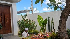 A courtyard with a dining setup featuring a table with a variety of dishes and a person seated. - JJ Villa 7 Ocean Blue (Badung)