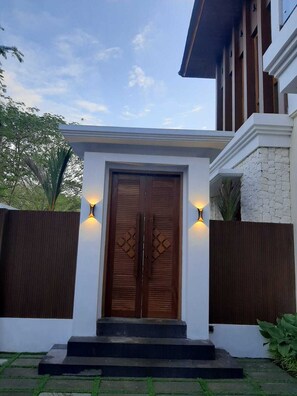 A modern building with a wooden double door, two wall-mounted lights, and a stone wall. - JJ Villa 7 Ocean Blue (Badung)