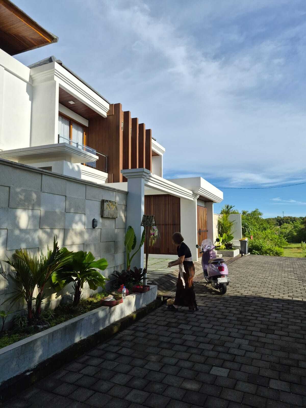 A modern house with a paved driveway and a person tending to a garden.