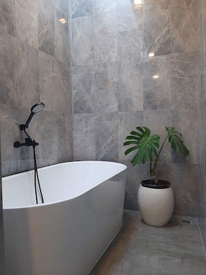 Un baño moderno con una bañera independiente, una planta en maceta y paredes de mármol.