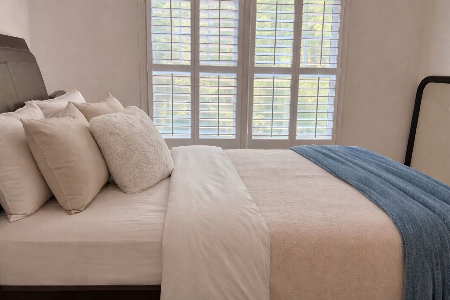 Ein Schlafzimmer mit einem Bett, Kissen, einer Decke und einem Fenster mit Jalousien.