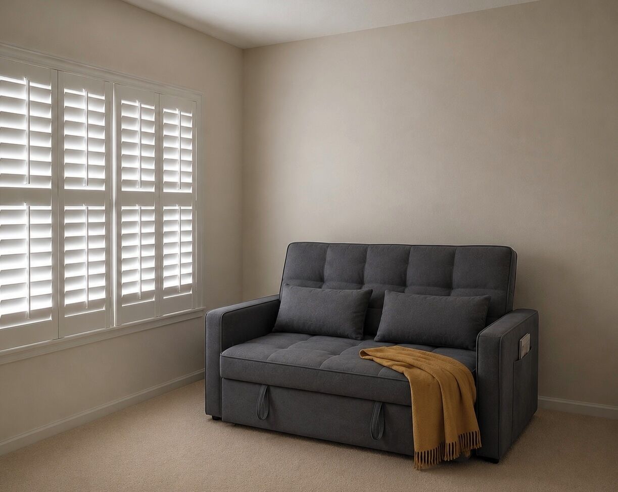 A gray sofa with a brown throw blanket, a window with blinds, and a plain wall.