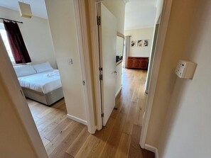 Et hotelværelse med en seng, trægulv, en dør og en gang, der fører til et andet værelse.