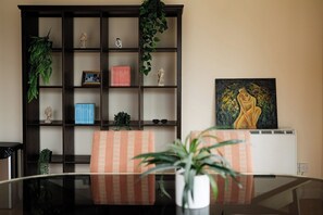 Ein Zimmer mit einem Glastisch, gestreiften Stühlen, einem dunklen Holzregal und einem Bild an der Wand.