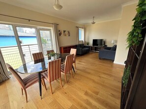 En moderne stue med et glasbord, sofaer, et fjernsyn og en balkon med udsigt.