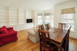 Una sala de estar moderna con una mesa de comedor de madera, un sofá rojo, un sofá color beige y un televisor montado en una pared blanca.