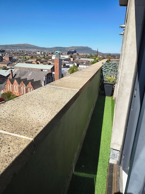 A balcony with a view of a town, a green artificial turf, and a building with a brick facade. - Bright City Centre Apartment and Stunning Views (Belfast)