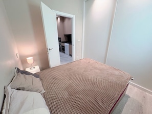Ein Schlafzimmer mit einem Bett, einem Nachttisch mit Lampe und einer Tür zu einer Küche.
