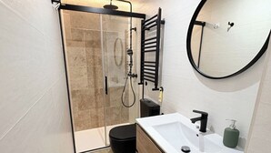 Et moderne badeværelse med en glasbrusekabine, et rundt spejl og en hvid vask med et træbord.