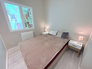 Ein Schlafzimmer mit einem Bett, zwei Nachttischen, einem Fenster mit Blick und einer Heizung.