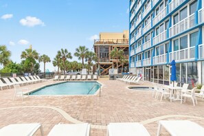 Ein Hotelpoolbereich mit mehreren Pools, Liegestühlen und einem Gebäude mit Balkonen.