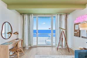 A room with a desk, chair, a tripod, a neon sign, and a balcony with a view of the ocean. - Penthouse 1BR + Bunk Room | Boardwalk | View Zone (Myrtle Beach)