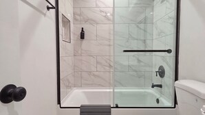Un baño moderno con ducha de vidrio, inodoro blanco y baldosas de mármol.