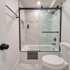 Ein modernes Badezimmer mit einer gläsernen Dusche, einer weißen Toilette und Marmorfliesen.