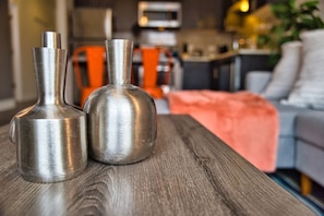 Two metallic vases on a wooden table in a living room with a sofa and a blanket in the background.
