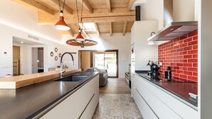 Une cuisine moderne dotée d’un îlot central, de luminaires suspendus et d’un mur de fond en briques rouges.