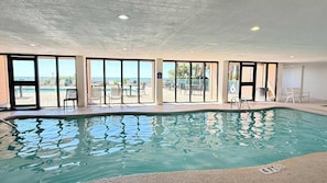 Ein Hallenbad mit freiem Blick ins Freie, großen Fenstern und einem Poolbereich mit Liegestühlen.