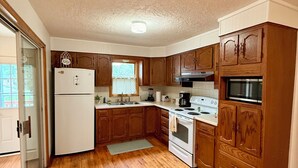 A kitchen with wooden cabinets, a white refrigerator, a stove, and a microwave. - Cozy 2-bedroom house in tranquil Excelsior Springs with AC (Excelsior Springs)