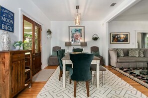 A dining area with a wooden cabinet, a table with chairs, a chandelier, and a painting on the wall. - Hackberry Haus | Hot Tub, Fire-pit, Pet Friendly w/ fee (Fredericksburg)