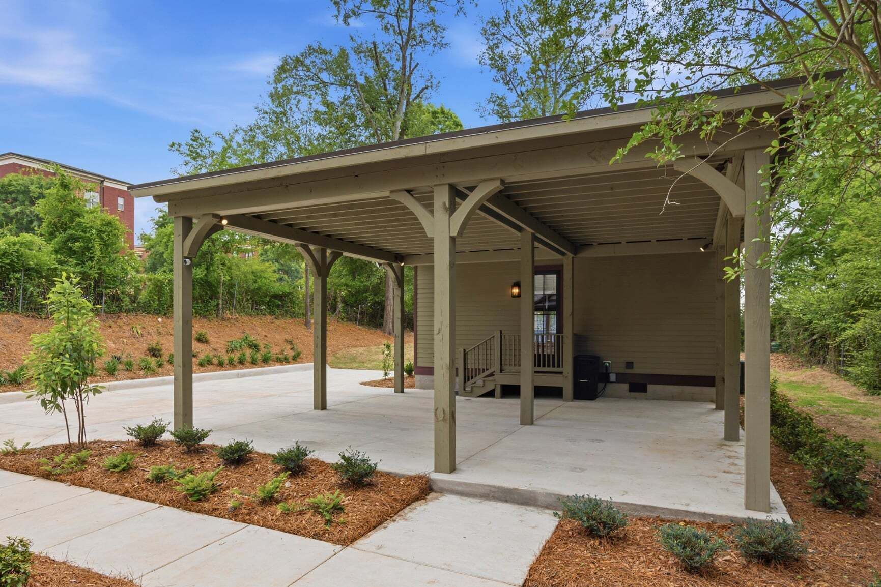 A covered outdoor area with a concrete floor, wooden pillars, and a small staircase leading to a door.