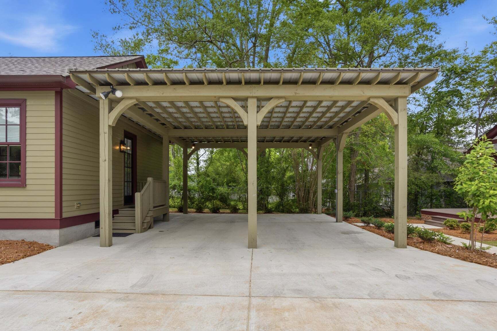 Un patio cubierto con suelo de hormigón, columnas de madera y una estructura de pérgola.