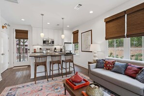 A modern kitchen with a central island, bar stools, and a dining area with a sofa and decorative pillows.