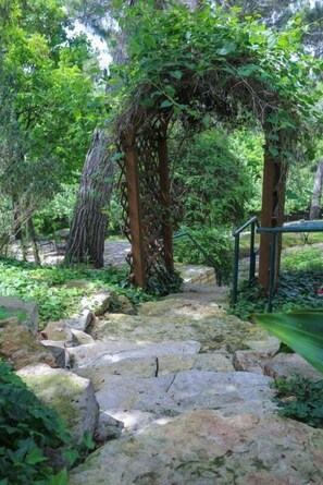 Ein steinbelagter Weg führt durch einen Garten mit einer mit Wein bewachsenen Holzpergola.