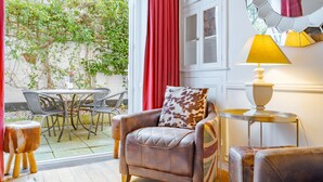 Una habitación con un sillón de cuero, una mesita redonda con lámpara, una mesa de comedor con sillas y vistas a un jardín a través de un ventanal.