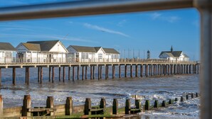 Un muelle con edificios, pilares de madera y una playa arenosa.