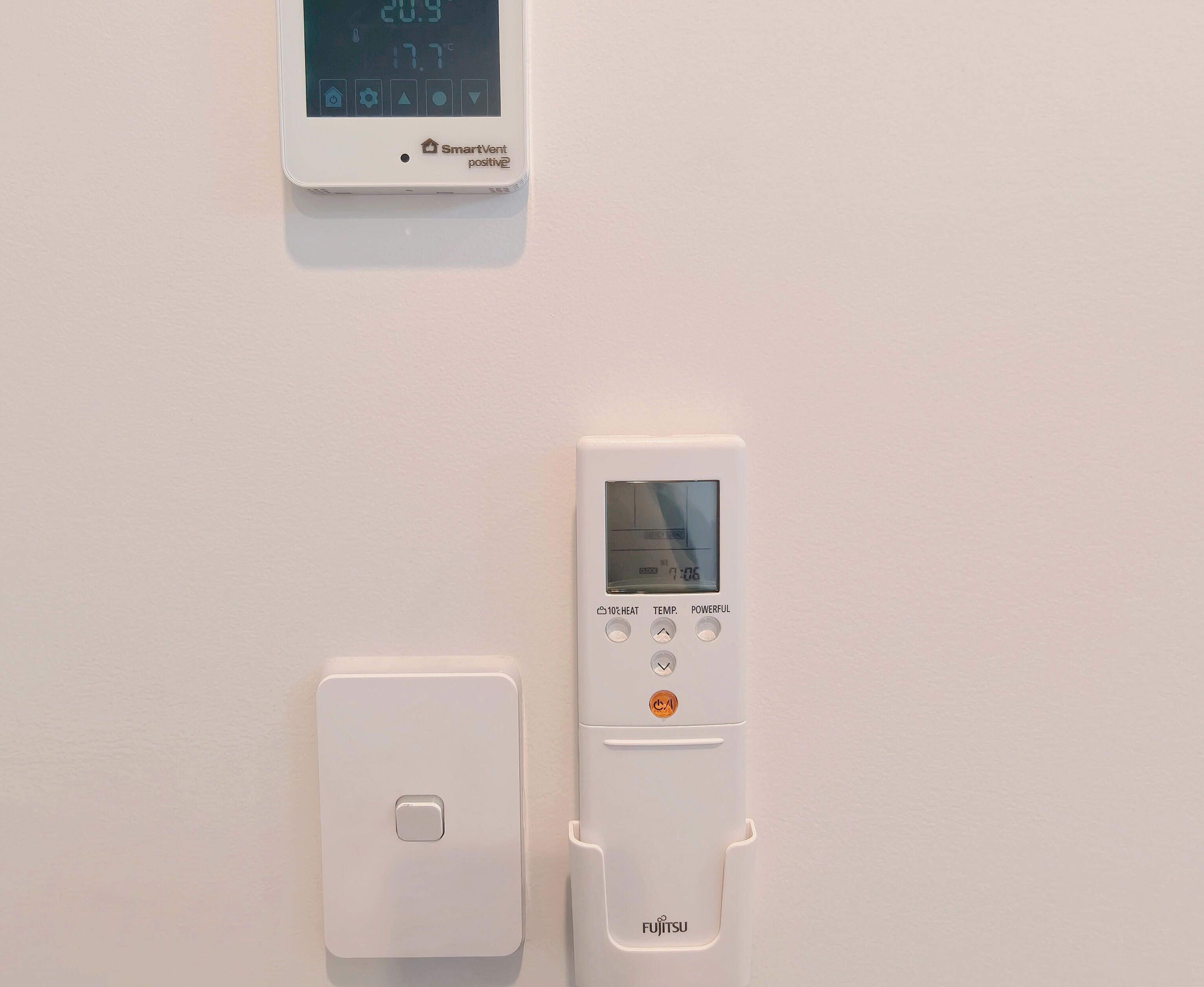 A wall-mounted thermostat with a digital display and control buttons.