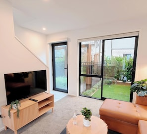 A modern living room with a flat-screen TV, wooden entertainment unit, and a sofa.