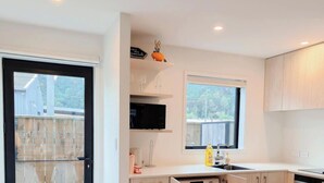 Een moderne keuken met een zwarte koelkast, een magnetron en een spoelbak. Twee ramen zorgen voor natuurlijk licht, en buiten is een houten schutting te zien.