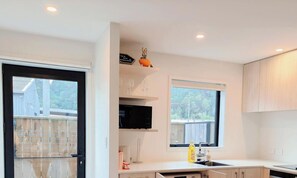Eine moderne Küche mit einem schwarzen Kühlschrank, einer Mikrowelle und einem Spülbecken. Zwei Fenster sorgen für natürliches Licht, und draußen ist ein Holenzaun zu sehen.
