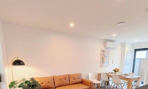 A modern living room with a sofa, dining table, chairs, and a lamp.