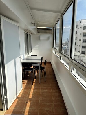 Ein schmaler Balkon mit Tisch und Stühlen, großen Fenstern und Blick auf Gebäude.