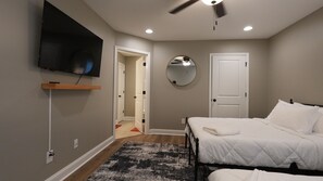 A bedroom with a bed, a TV mounted on the wall, a ceiling fan, and a door leading to another room.