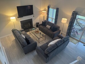 Un salon avec une cheminée, deux canapés, une table basse et un téléviseur fixé au-dessus de la cheminée.