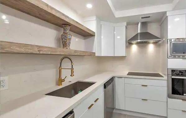 Une cuisine moderne avec des meubles blancs, un évier en acier inoxydable, un four encastré et un vase décoratif posé sur l’étagère.