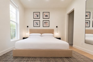 A modern bedroom with a large bed, two bedside tables, a wall-mounted mirror, and framed artwork. - Urban Casa at Olmos Park (San Antonio)