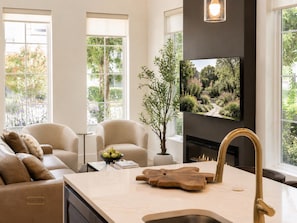 A modern living room with a sofa, chairs, a fireplace, and a large window with a view of a garden. - Urban Casa at Olmos Park (San Antonio)