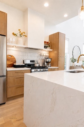 A modern kitchen with a marble island, wooden cabinets, and stainless steel appliances. - Urban Casa at Olmos Park (San Antonio)