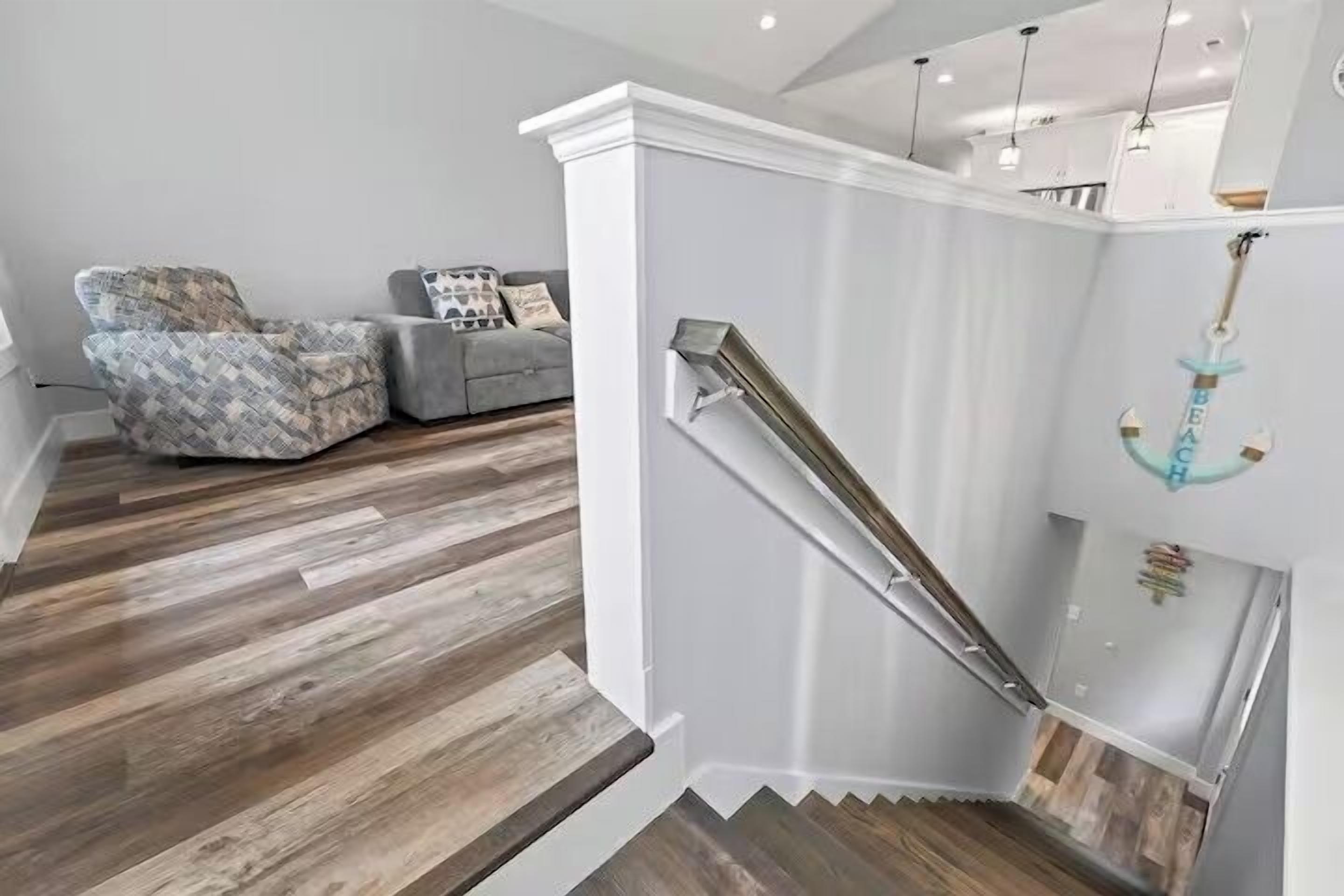 Eine Treppe mit Metallgeländer, Holzboden, einem grauen Sofa und einer Wanddekoration als Anker.